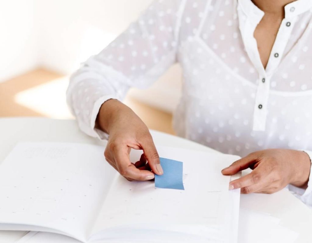 this is a picture of a women putting a sticky note in a planner